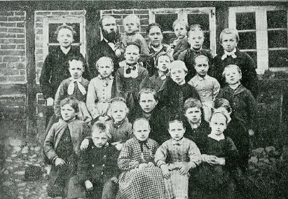Evald Tang Kristensen, hans hustru og to brn (i baggrunden) samt skolebrnene i Farup skole,  1876.